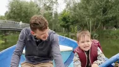 可爱的小男孩握着桨，帮助他年轻的父亲划船。 快乐的年轻父亲和他的小儿子玩得很开心。 可爱的小爸爸